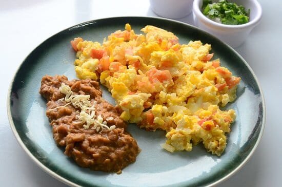 Huevos al gusto con jamón y frijoles refritos, acompañados de tortillas de maíz. Desayuno tradicional con huevos frescos y sabor casero de calidad. Rico fresco y natural.