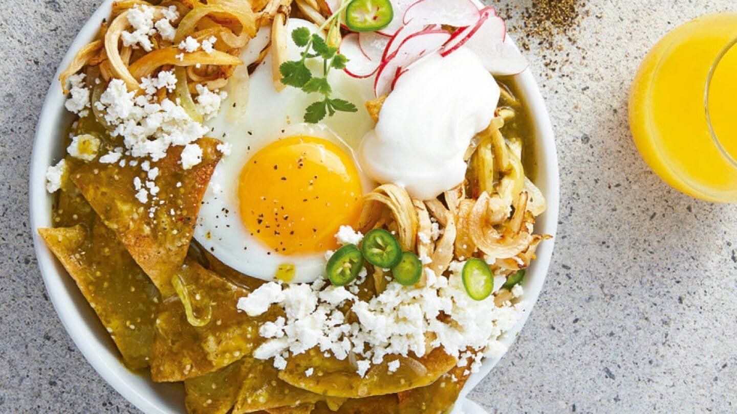 Chilaquiles verdes con salsa verde, queso fresco, pollo deshebrado y tortillas de maíz, acompañados de cebolla morada y cilantro fresco. Desayuno mexicano con ingredientes de calidad y sabor auténtico.