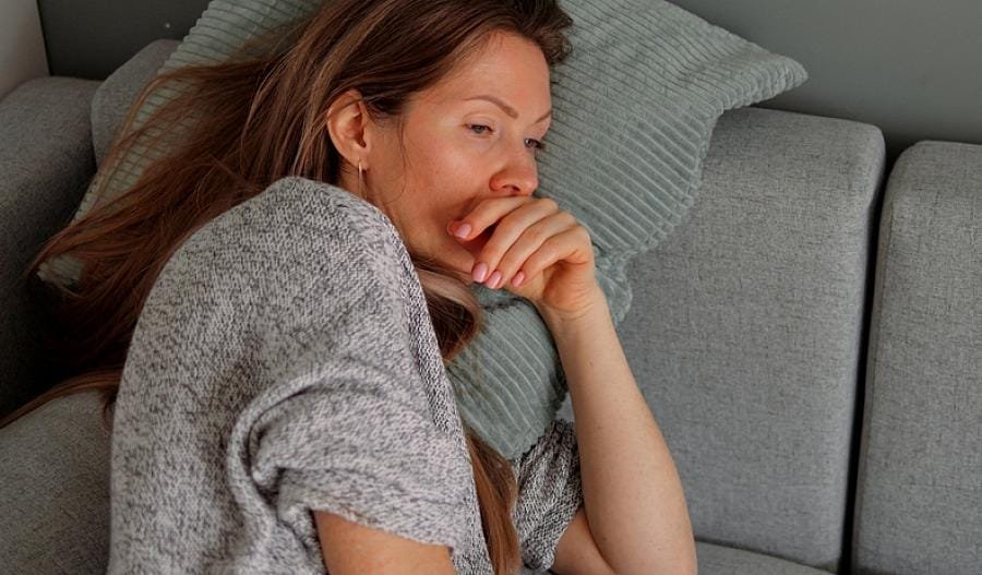 Mujer descansando en el sillón, sintiendo los efectos de la gripe. El descanso es esencial para permitir que el cuerpo se recupere mientras se combate la congestión y los síntomas comunes de la gripa. Disfrutar de bebidas calientes como té de jengibre con limón o jugos naturales puede ayudar a aliviar la tos y mejorar la circulación, promoviendo una recuperación más rápida.